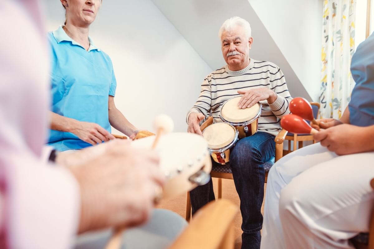 Älterer Mann mit einer Trommel in der Hand, der in einem Sitzkreis mit weiteren Menschen mit Instrumenten in der Hand sitzt